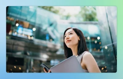 A woman holding a mobile phone and some files in both hands, looking somewhere.