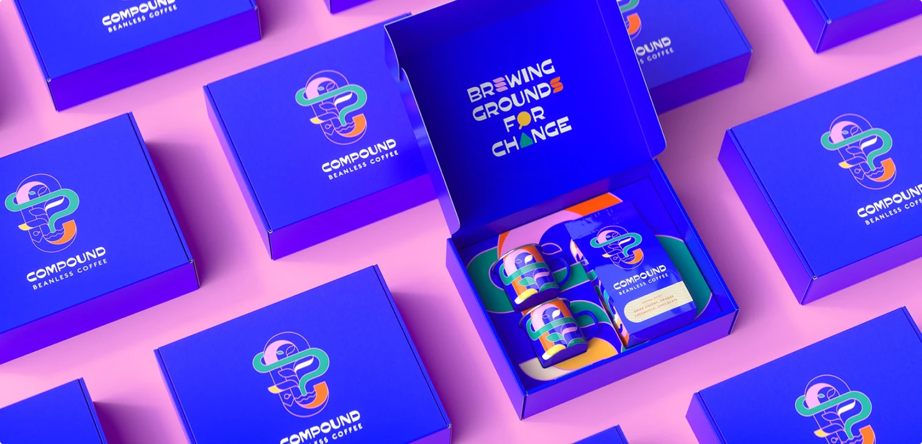 Multiple vibrant cobalt blue boxes for Compound Beanless Coffee arranged on a pink background. One open box reveals colorful packaging contents. The boxes feature the Compound logo and tagline "BREWING GROUNDS FOR CHANGE" in white text, showcasing bold design and sustainability messaging.